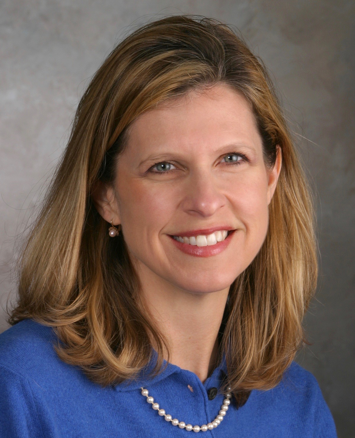 A blond woman in a blue shirt with pearls